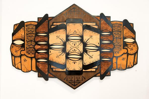 The GATS geometric wall sculpture displays abstract faces with closed eyes, intertwined patterns, and earthy hues of brown, black, and tan. Crafted in enamel on wood, the layered design brings dynamic movement and depth.