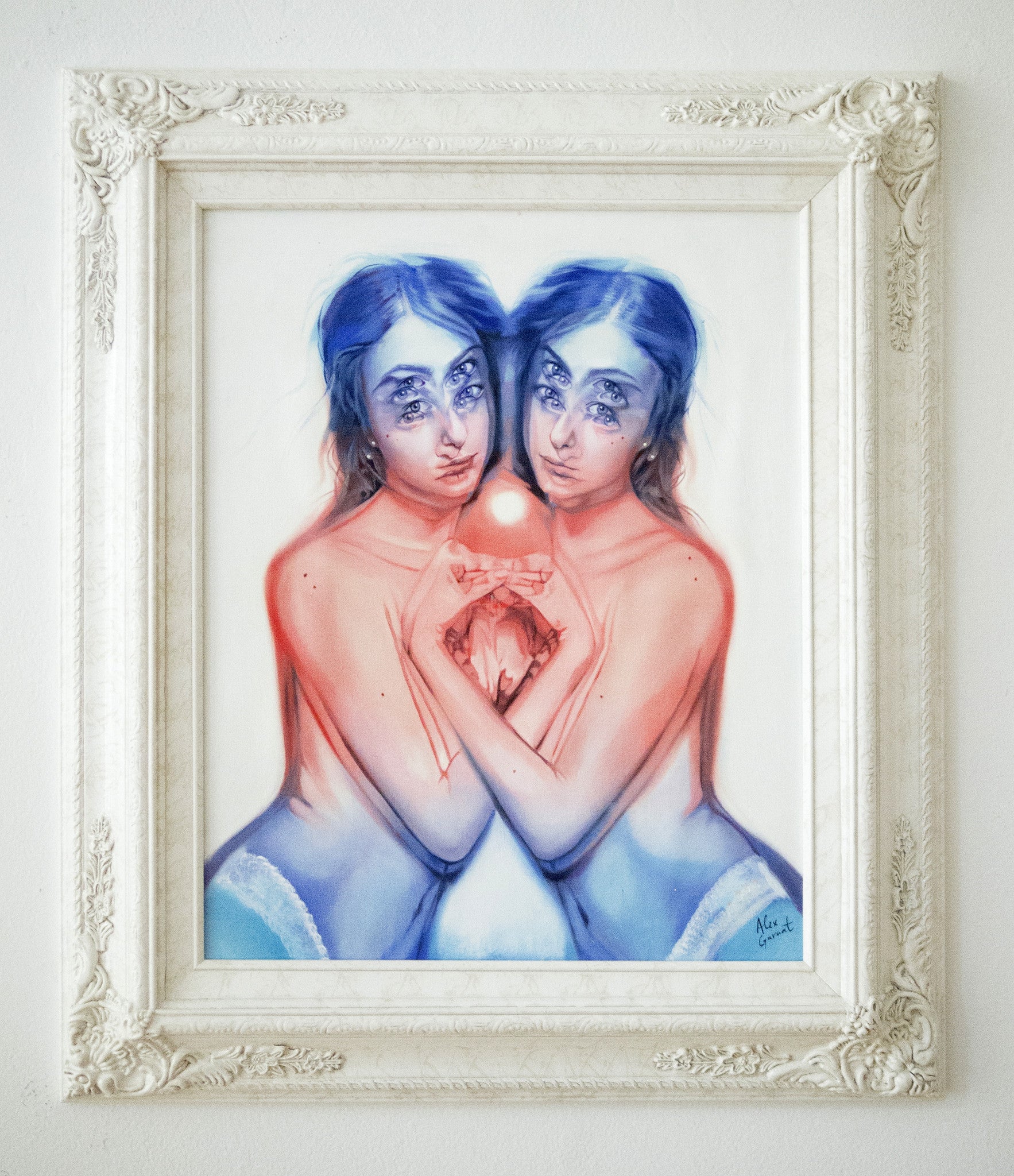 Artwork by Alex Garant features two mirrored figures with interconnected arms, using blue and red tones for a symmetric, make-believe realm. The abstract facial details enhance the ethereal mood, framed in ornate white.