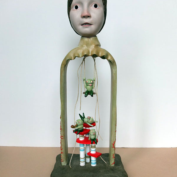 Surreal resin sculpture by Doubleparlour: a large human-like head on slender legs with whimsical frog figures hanging over pillars and mushrooms. Hand-sculpted and painted with acrylics, the background is plain.
