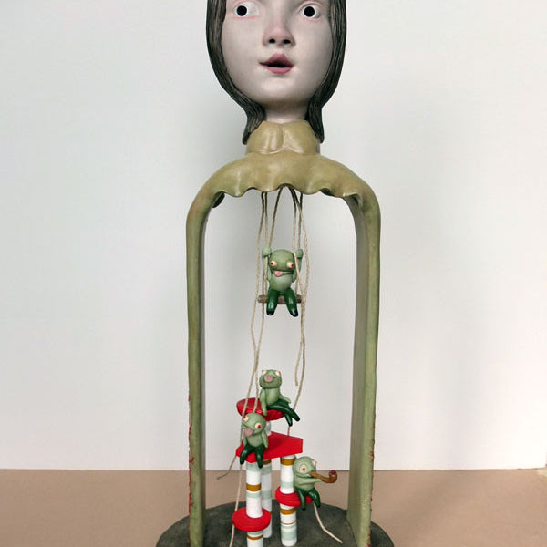 The Doubleparlour whimsical resin sculpture features a large head with wide eyes on a slender frame. Small green figures hang on strings, interacting with red and white elements at the base. Varnish and acrylic paint add to its playful appeal.