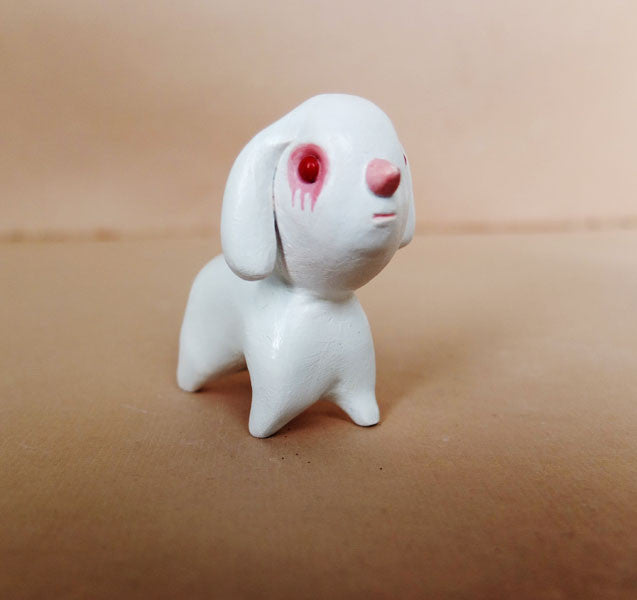A hand-sculpted Doubleparlour piece, this small white resin dog with long ears and a pink nose stands on a brown surface. Its round eyes, softly shaded in pink and detailed with acrylic, exude an expressive charm.