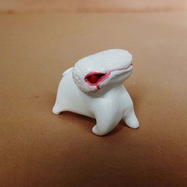 A small white figure with a round body, short legs, and a long head featuring a pink-red eye stands against a brown backdrop. Hand sculpted from resin and painted with acrylics, this exquisite piece is crafted by Doubleparlour.