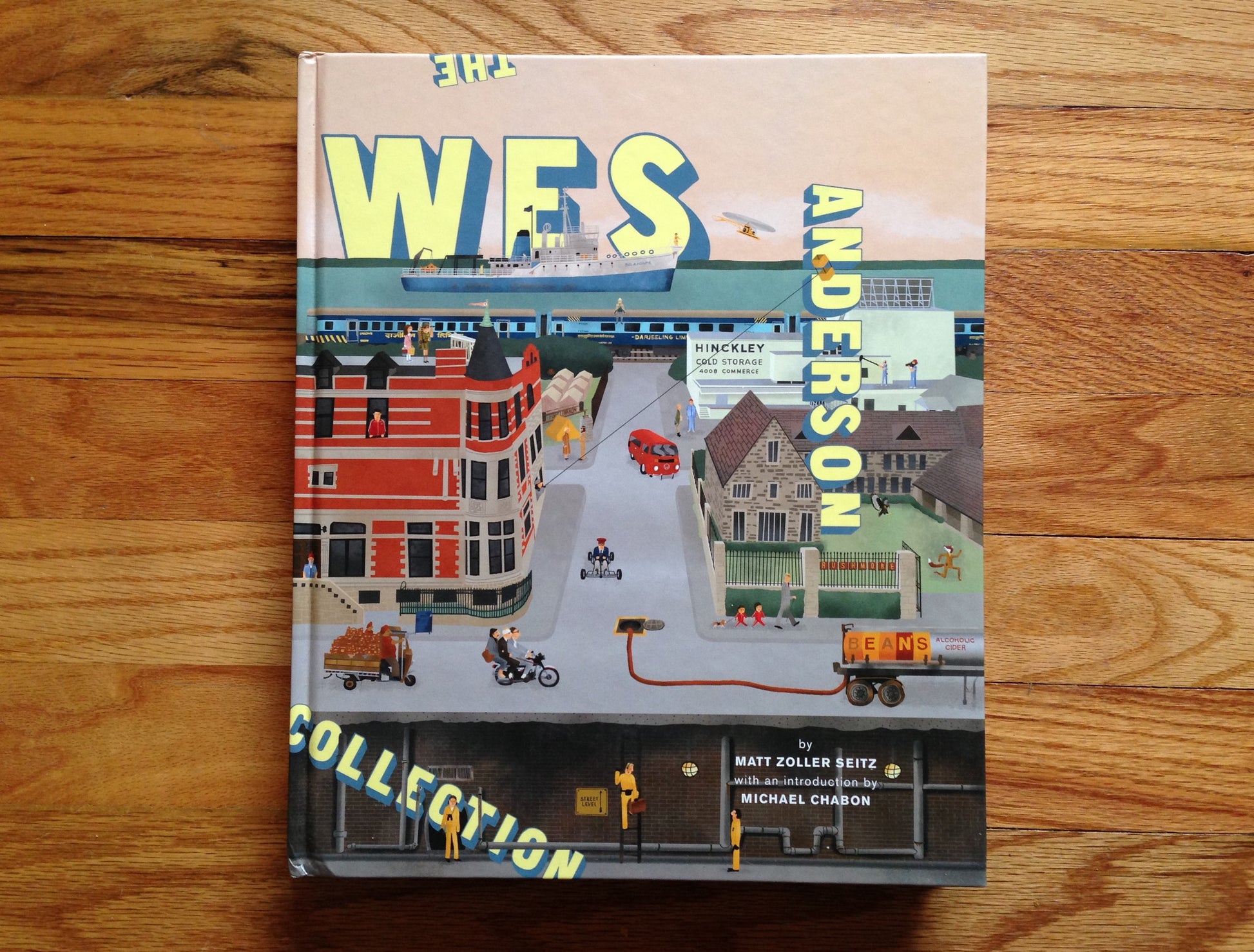 Matt Zoller Seitzs The Wes Anderson Collection features a whimsical cityscape cover with buildings, vehicles, and characters that encapsulate Andersons unique style and explore his films with behind-the-scenes photos.