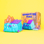 A vibrant limited edition Dumpster Fire vinyl figure by 100% Soft, featuring a blue dumpster with purple accents and cartoon flames, sits beside its box on a bright yellow background.
