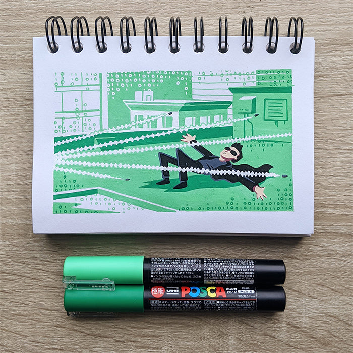 A James Chapman notepad drawing features a person in sunglasses dodging zig-zag lines like The Matrix, with binary code behind. Two green paint pens are placed below the notepad.