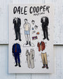 Brighton Ballard illustrated Dale Cooper paper doll sheet featuring a doll in underwear and various outfits, accessories, and faces to mix and match, all set against a white wood background—an original design.