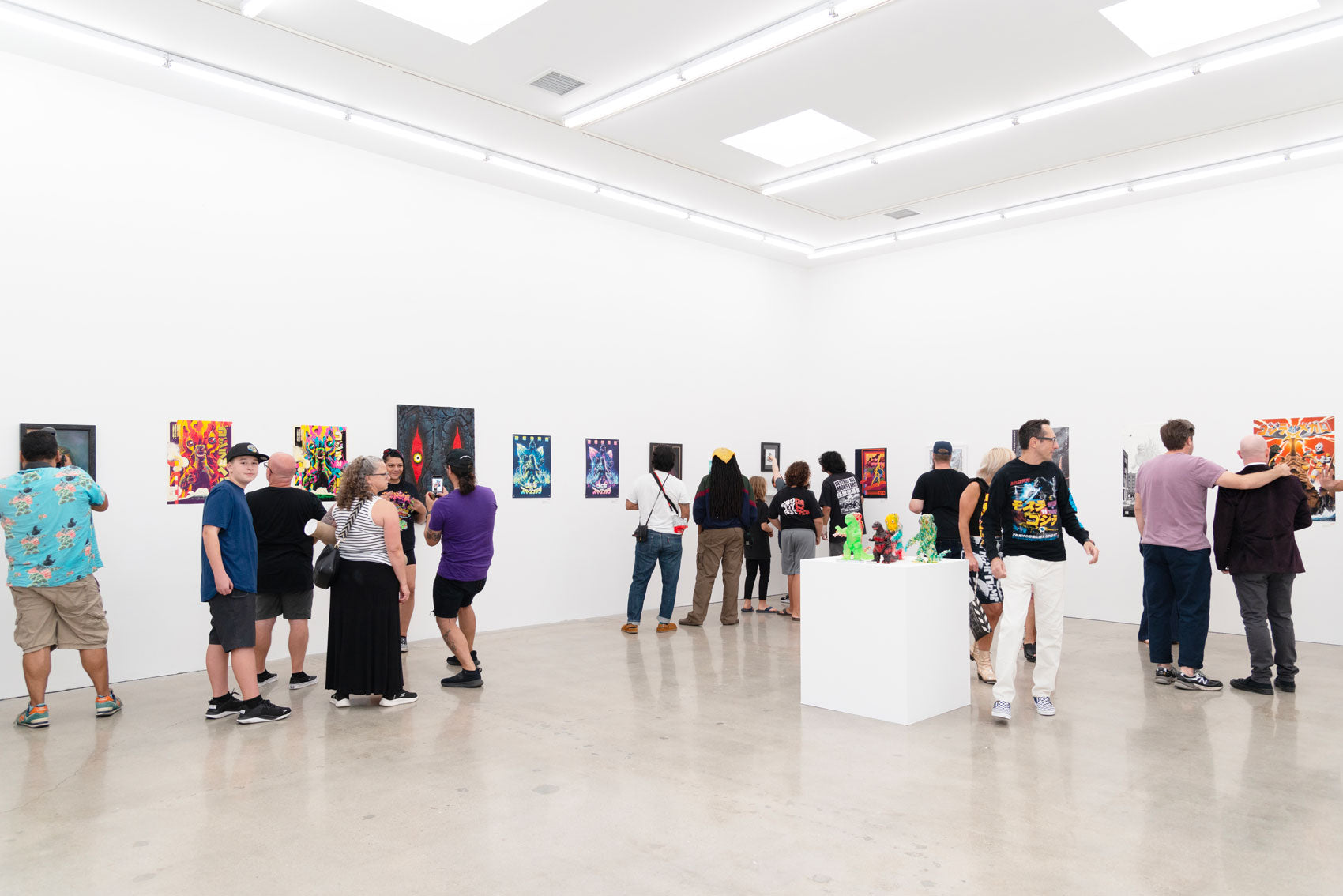 A group of people in an art gallery with colorful paintings on white walls. Visitors are looking at the artwork, and a sculpture is displayed on a pedestal in the center. The room is brightly lit with a polished floor.