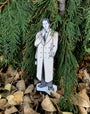 Cardboard cutout of a man in a coat standing among green foliage and fallen leaves.