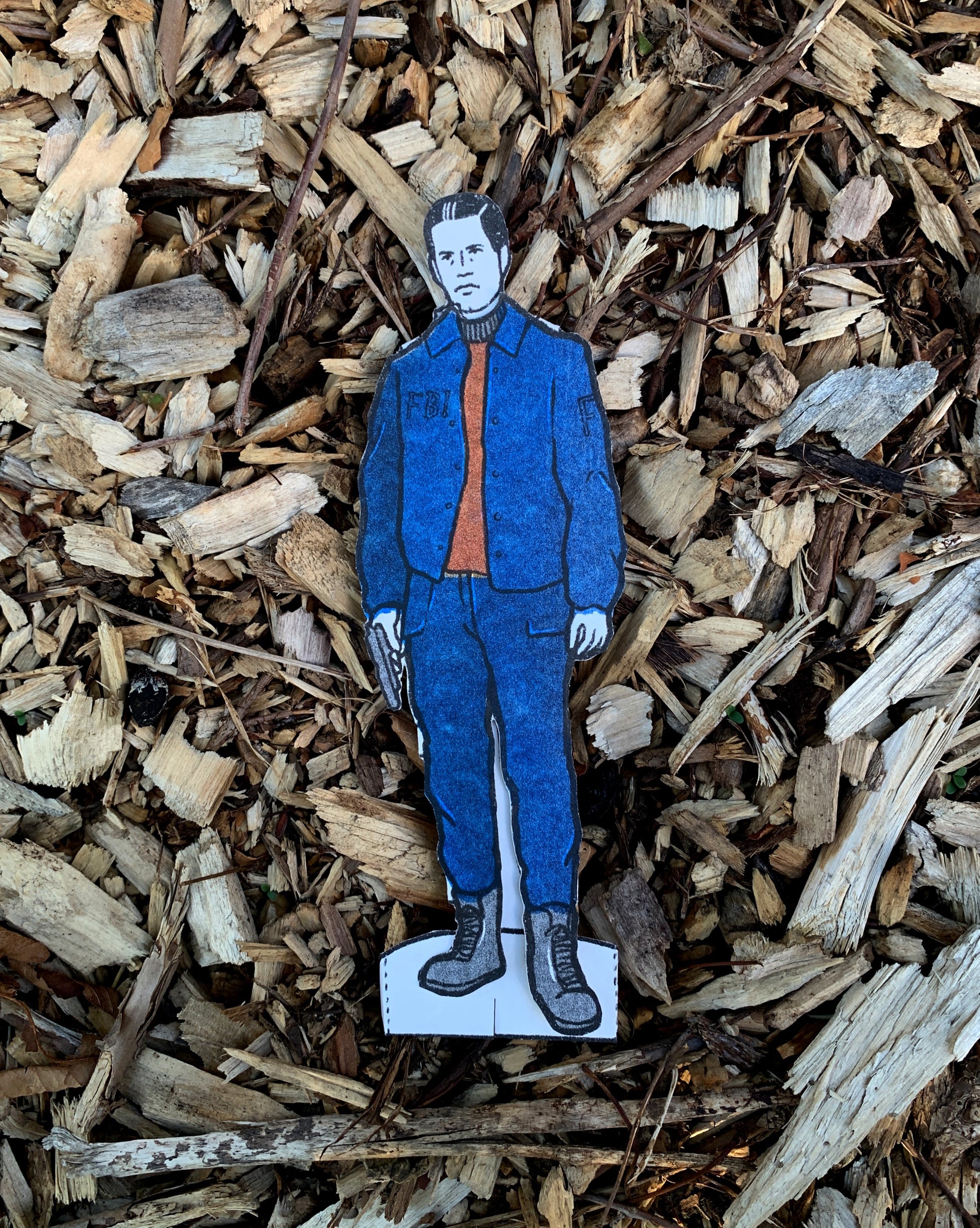 Cardboard cutout of a person in blue jacket and orange shirt on wood chips