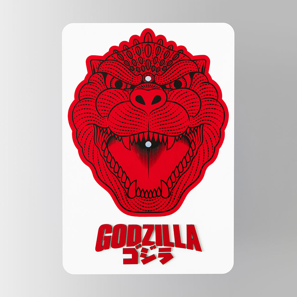 The backing of a mixed media sculpture of an enlarged enamel pin of godzilla's head 