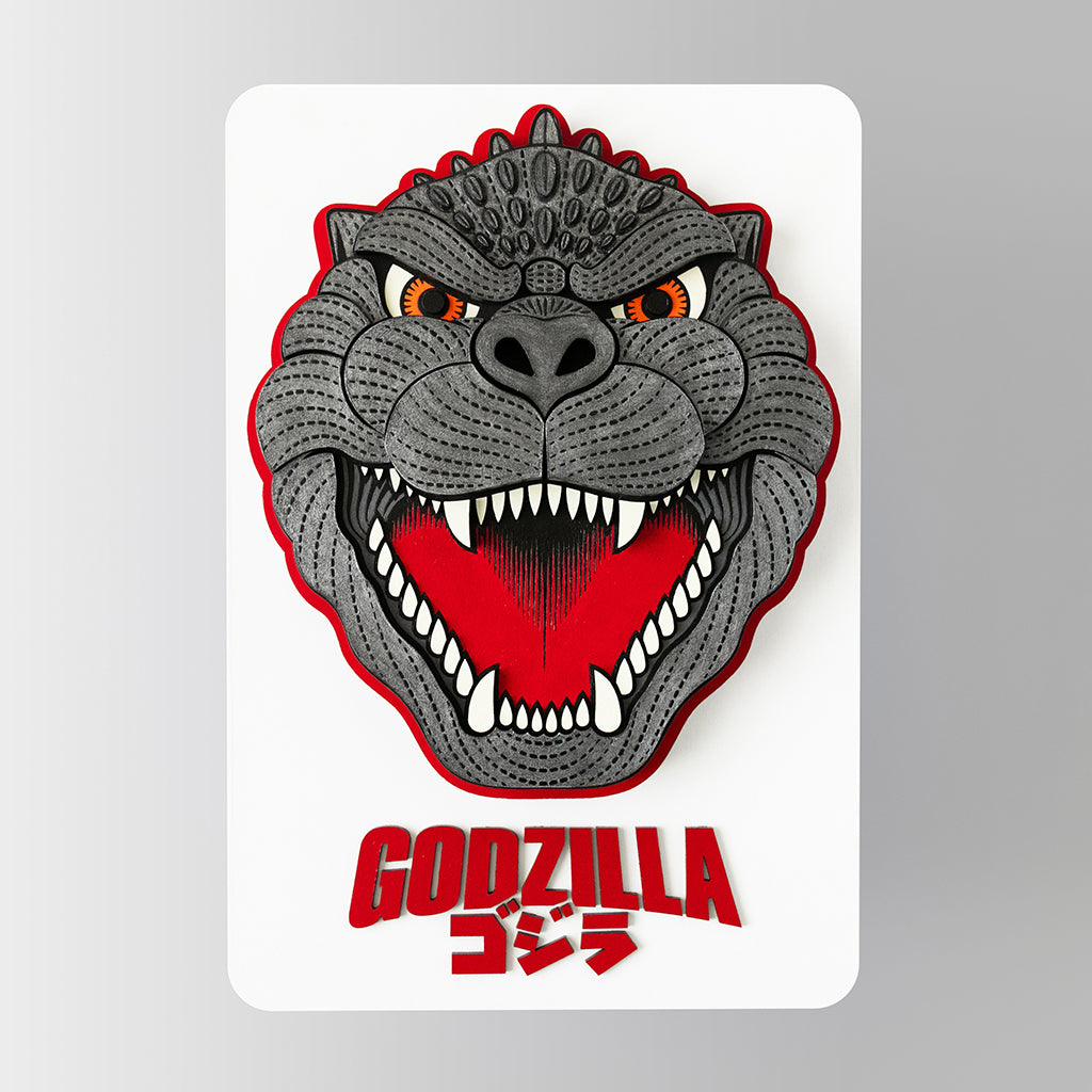 Mixed media sculpture of an enlarged enamel pin of Godzilla's face on a white backing with the Godzilla logo in red underneath the pin