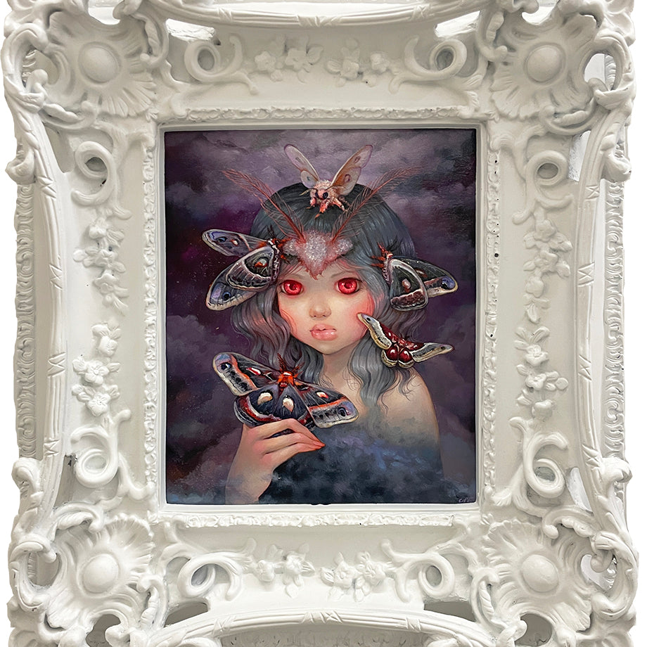 A Spoke Art framed painting in Camilla d'Errico's style shows a girl with large red eyes and dark, wavy hair among colorful moths. The ornate white floral frame enhances the mysterious, surreal vibe of Prophet Of The Night.