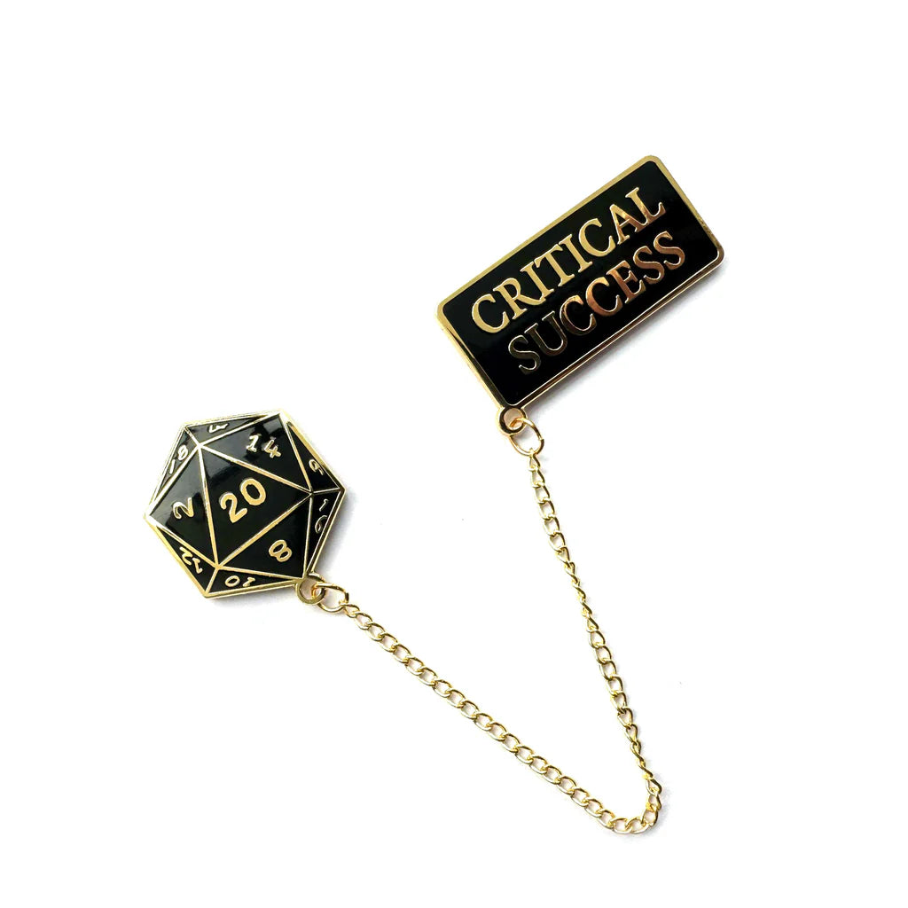 The Spoke Art black and gold-plated hard enamel pin set features a 20-sided die showing 20 connected by a gold chain to a rectangular pin with CRITICAL SUCCESS in gold letters.