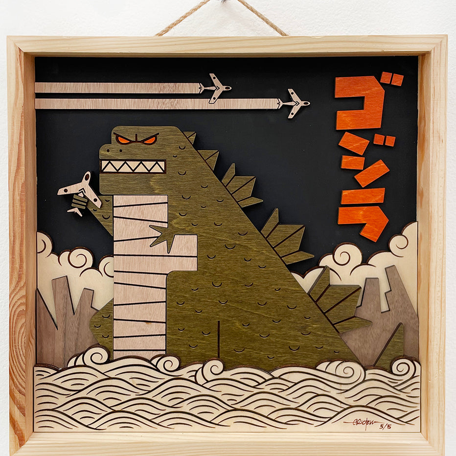 Image created from wood of Godzilla holding an airplane in the water with a black background and two airplanes flying above him