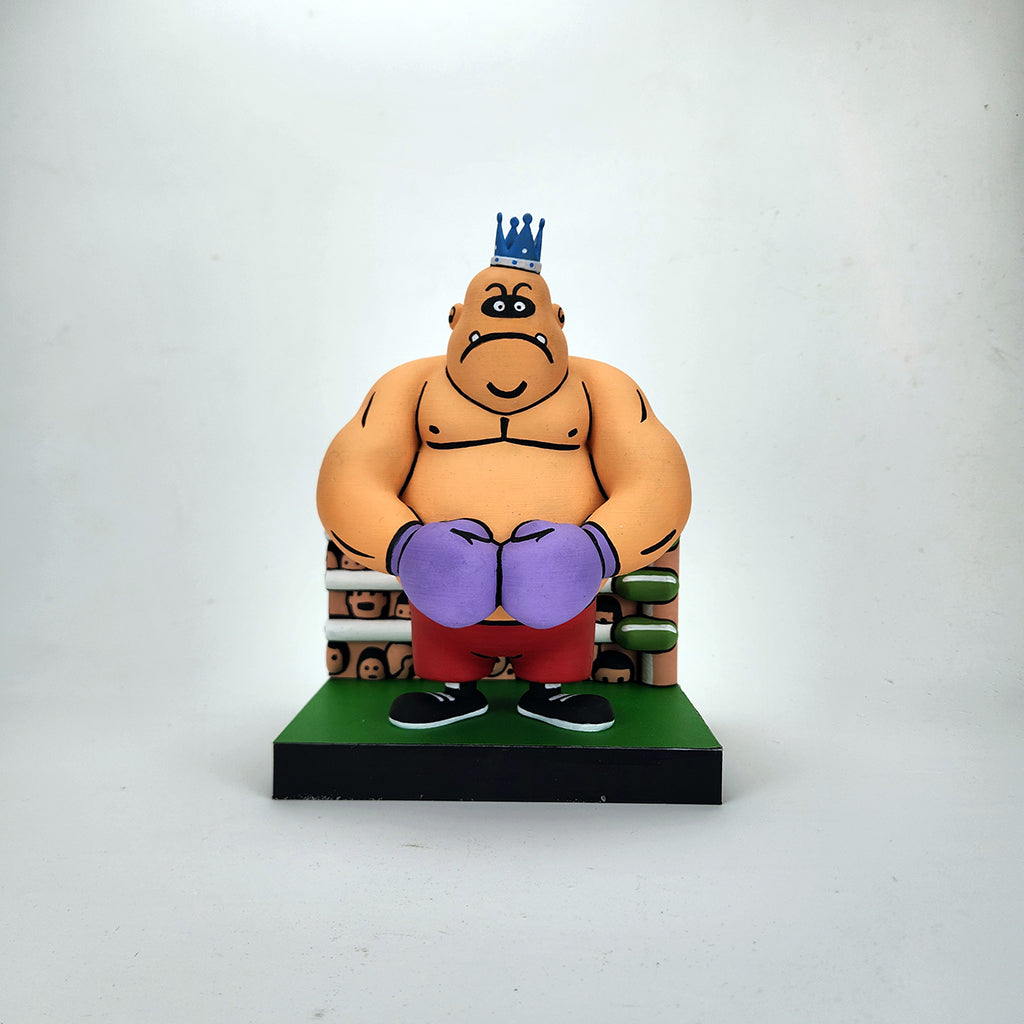 A cartoonish Geoff Trapp figurine of a muscular boxer wearing a crown, purple gloves, red shorts, and black shoes sits on a bench against a plain white background, inspired by King Hippo art from Mike Tyson's Punchout.