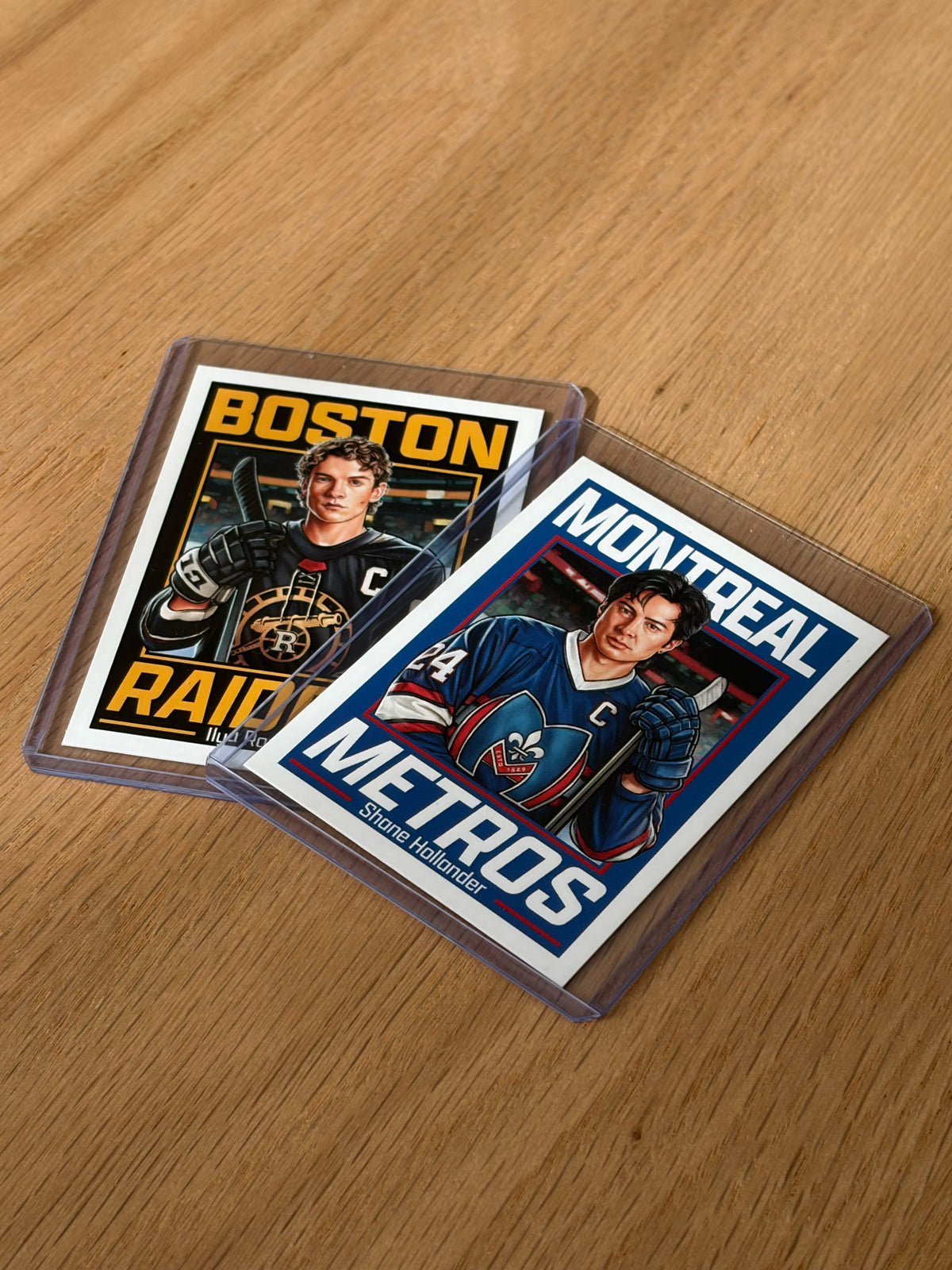 Two hockey trading cards from the Culyer Smith trading cards Heated Rivalry set, each in protective sleeves, are lying on a wooden surface. One card reads Boston Raiders and the other Montreal Metros, each showing a hockey player in uniform holding a hockey stick. This signed numbered edition perfectly captures the spirit of classic competition.