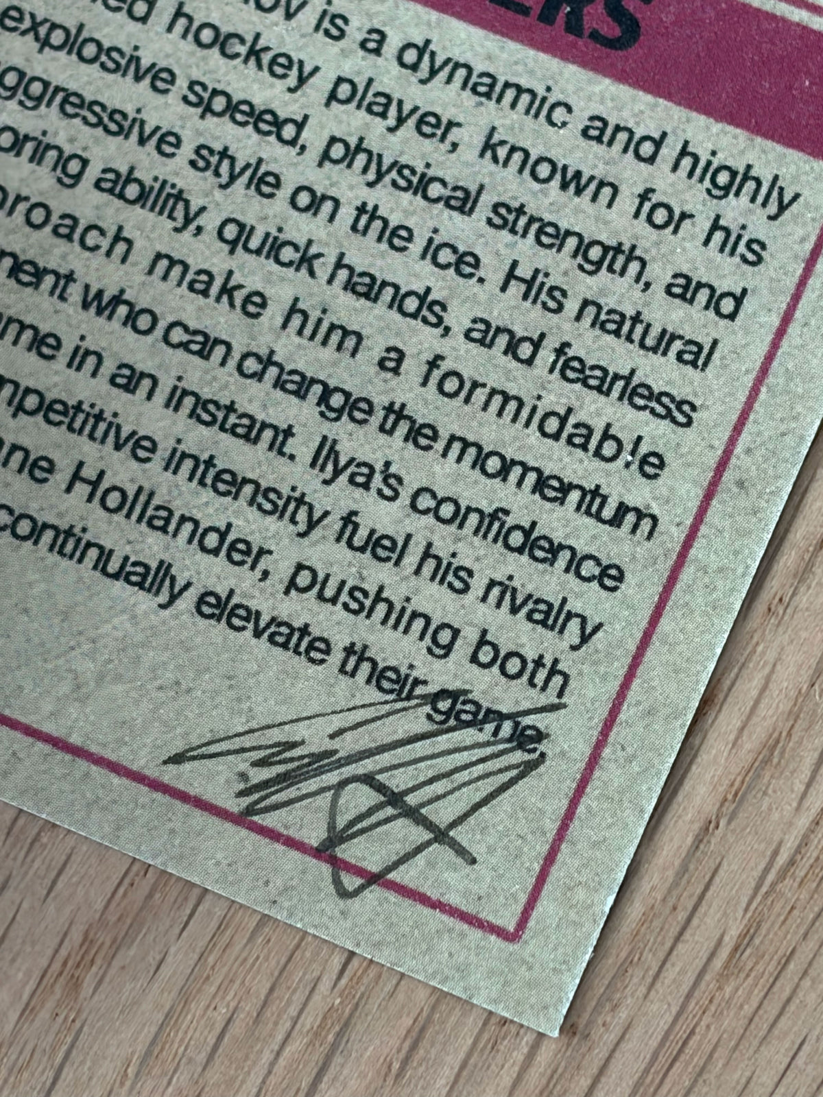 A close-up of a printed card from the Culyer Smith trading cards, with black text describing a hockey player, featuring a black autograph at the bottom on textured paper next to a wooden surface.