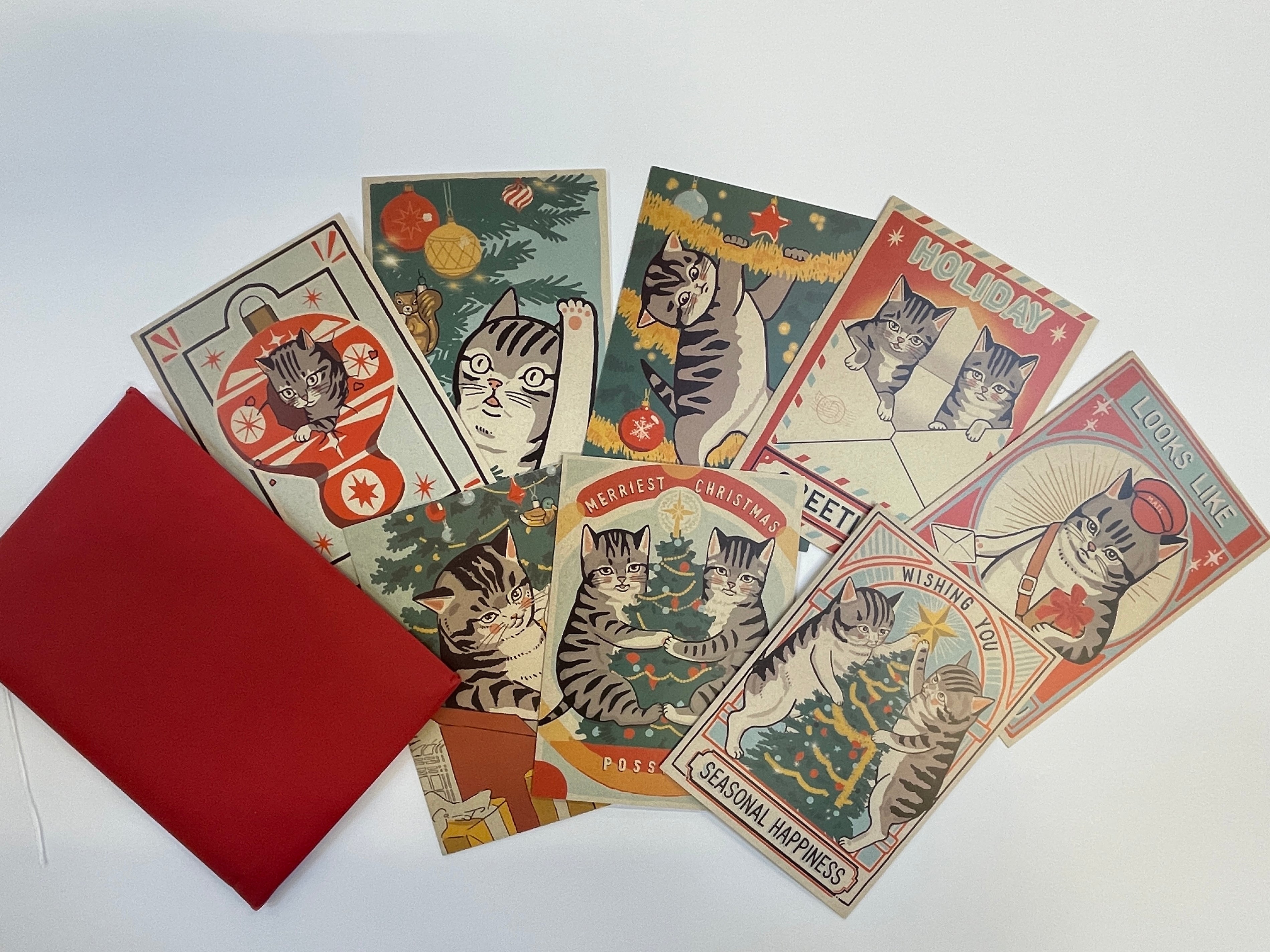 A set of six Arna Miller vintage-style cat Christmas cards, featuring playful tabby cats in festive scenes, is displayed with a red envelope on a white background.