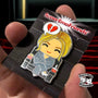 A hand holds a Super Emo Friends limited edition hard enamel pin showing a cartoon character with blonde hair in a striped suit, sitting in a chair holding a drink, beneath a broken heart and the “SuperEmoFriends” text.
