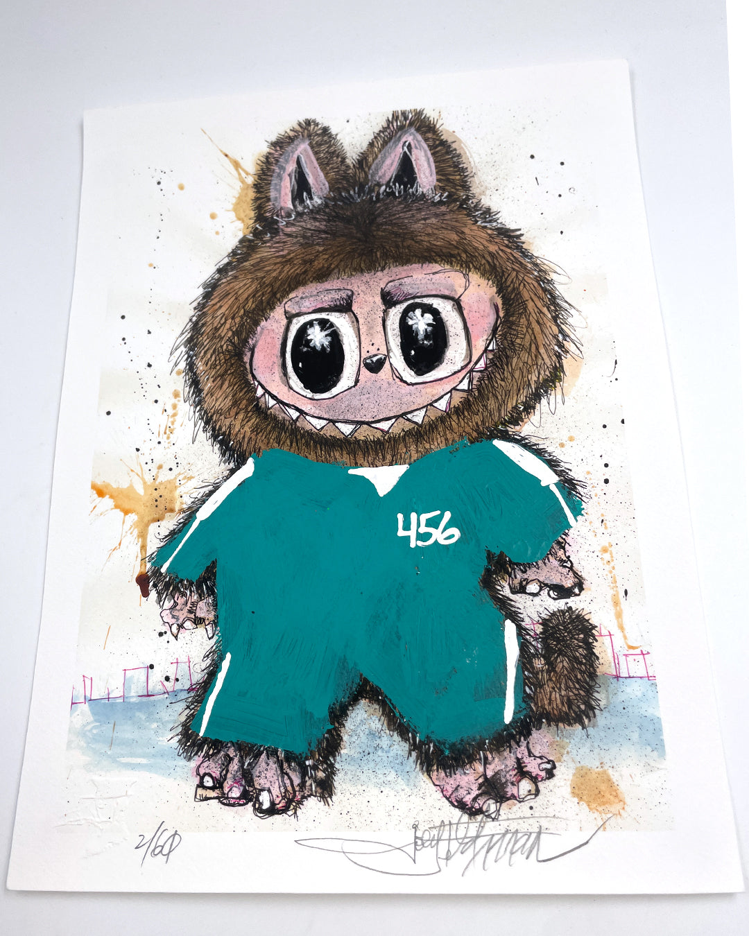 A whimsical Joey Feldman archival pigment print depicts a big-eyed, furry creature in a teal tracksuit numbered 456. Bear-like ears, claws, and a toothy grin stand out amid hand-painted embellishments and a paint-splattered background.