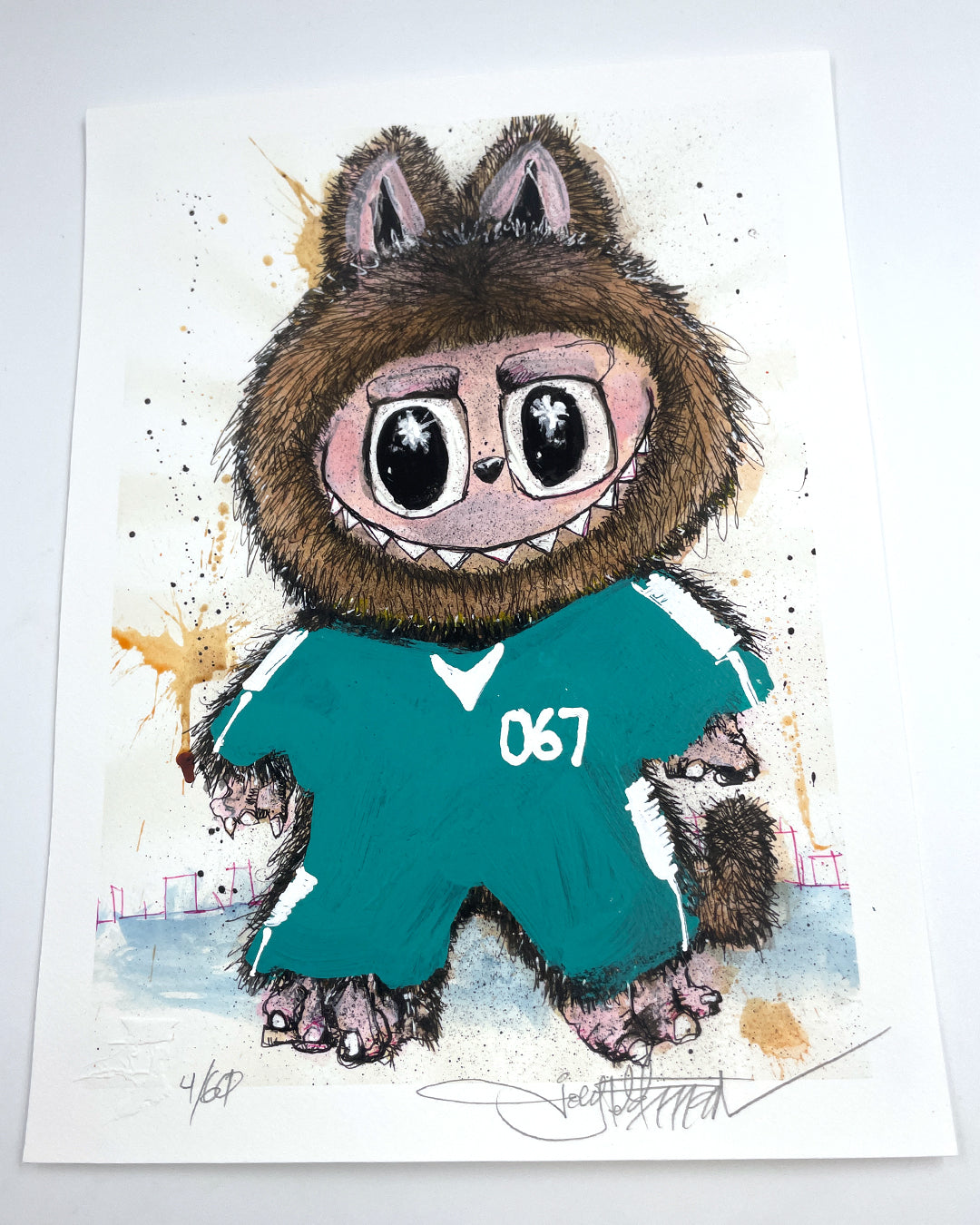 A whimsical archival pigment print by Joey Feldman depicts a furry creature in a teal outfit numbered 067, with large eyes, sharp teeth, and animal-like traits. Each print is signed and numbered in the corners.