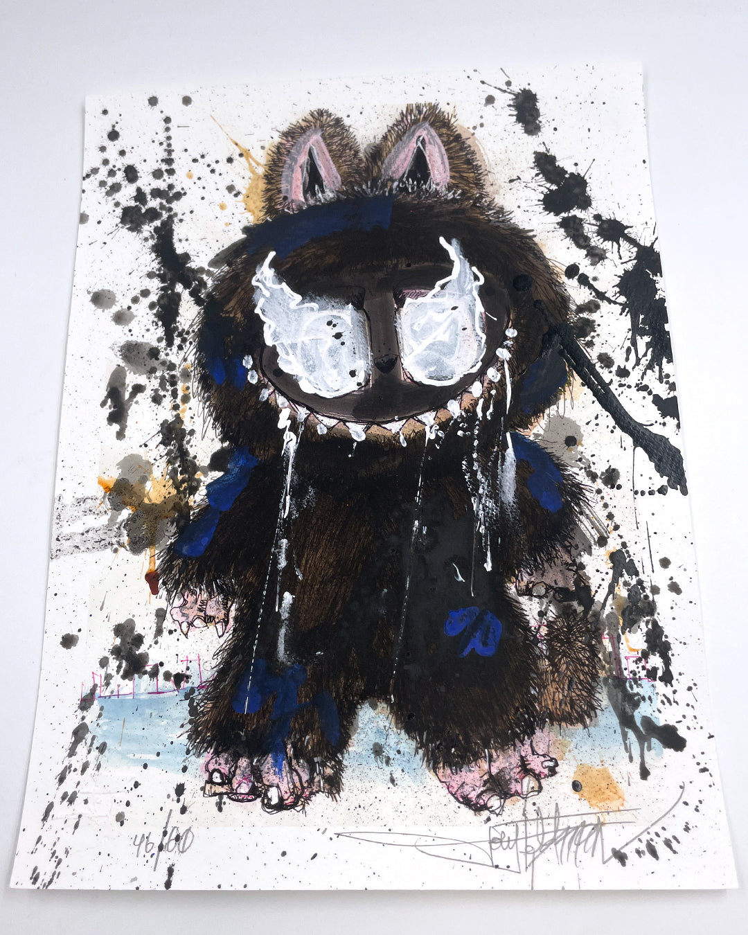 A Joey Feldman-inspired textured illustration features a furry, blue and black monster with large white eyes, sharp teeth, and drool, set against splattered paint on white paper.