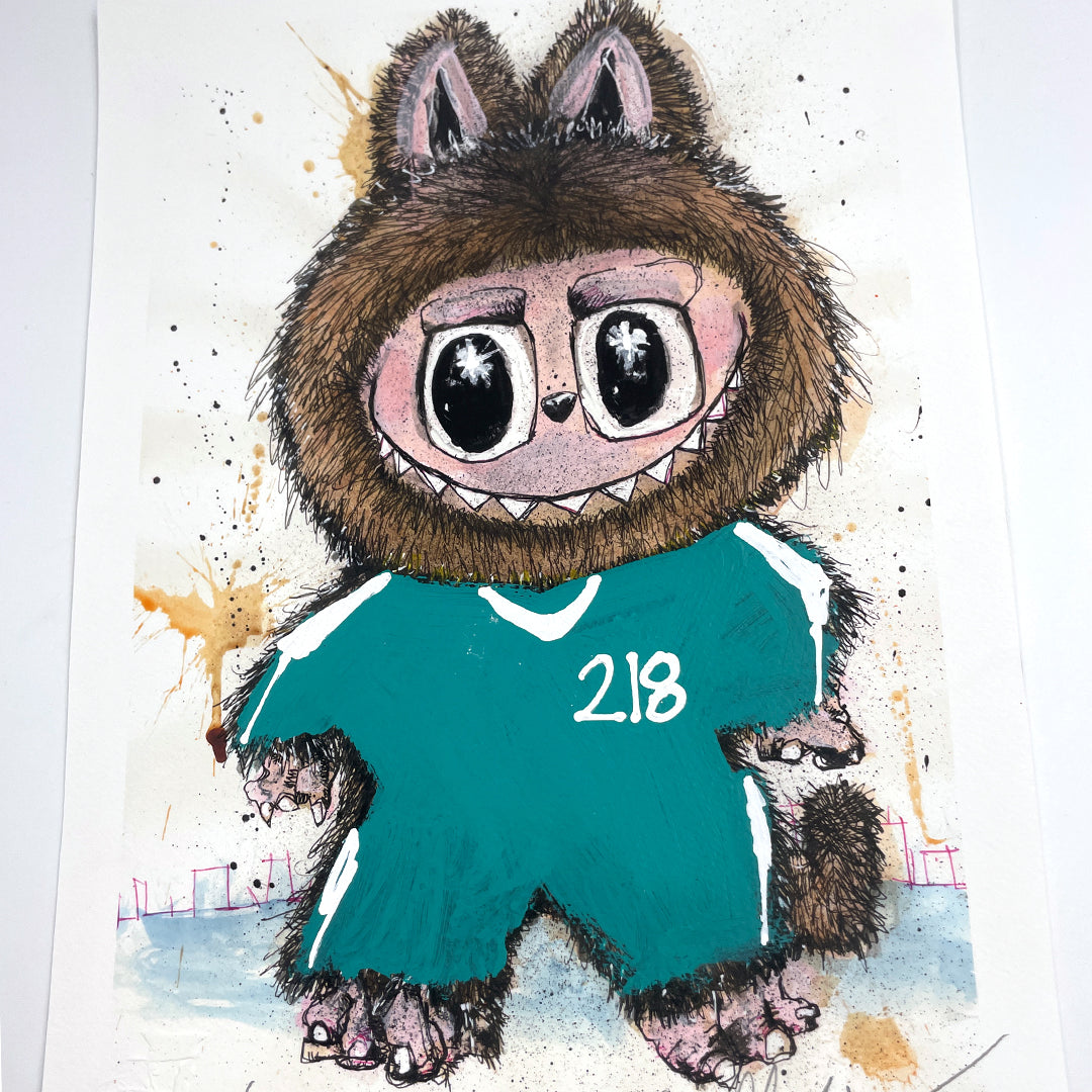 A cartoon character with big eyes, a wolf-like hood, sharp teeth, and a green tracksuit labeled 218 is set on a splattered background in this signed and numbered Joey Feldman archival pigment print.
