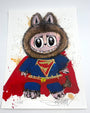 A cartoon creature in a furry animal costume with pointy ears, big eyes, and a red superhero cape and S-emblem suit. The background features Joey Feldman-inspired paint splatters and hand-painted embellishments. Brand: Joey Feldman.