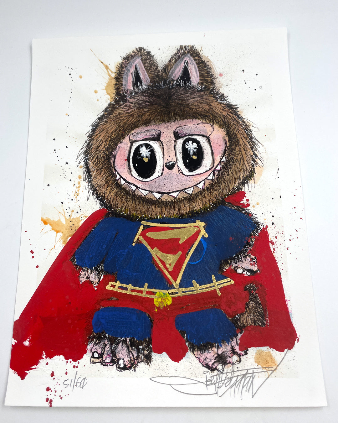 A cartoon creature in a furry animal costume with pointy ears, big eyes, and a red superhero cape and S-emblem suit. The background features Joey Feldman-inspired paint splatters and hand-painted embellishments. Brand: Joey Feldman.