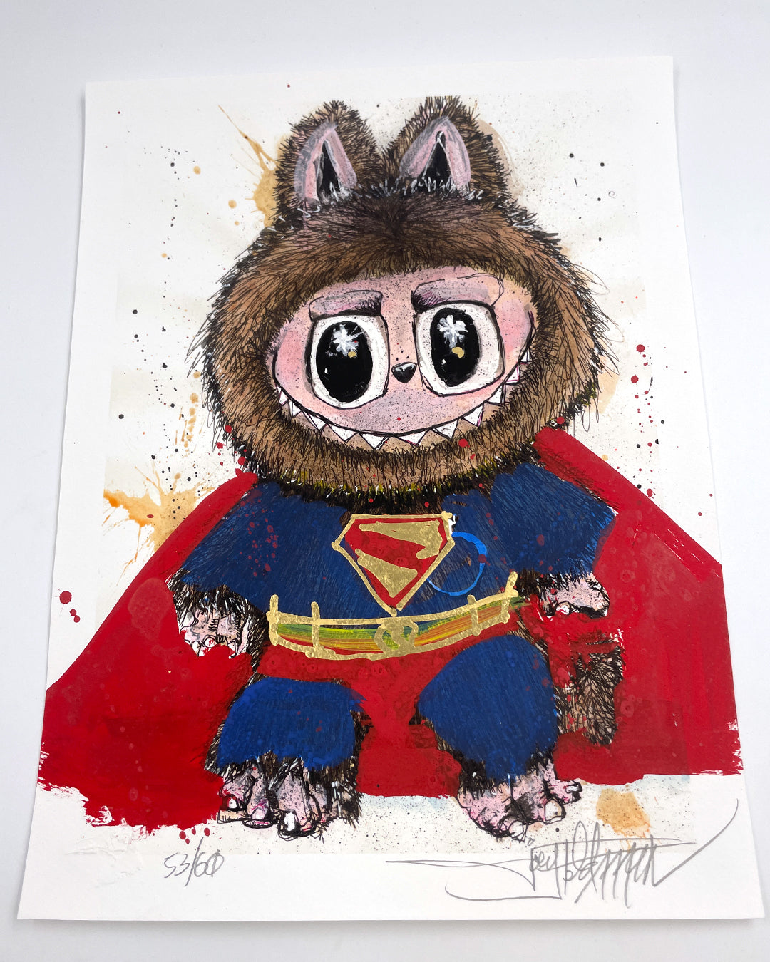 Joey Feldman-inspired illustration of a cute, wide-eyed creature in a Superman costume with a furry hood and bear ears, seated on a white background with colorful paint splatters and hand-painted details.