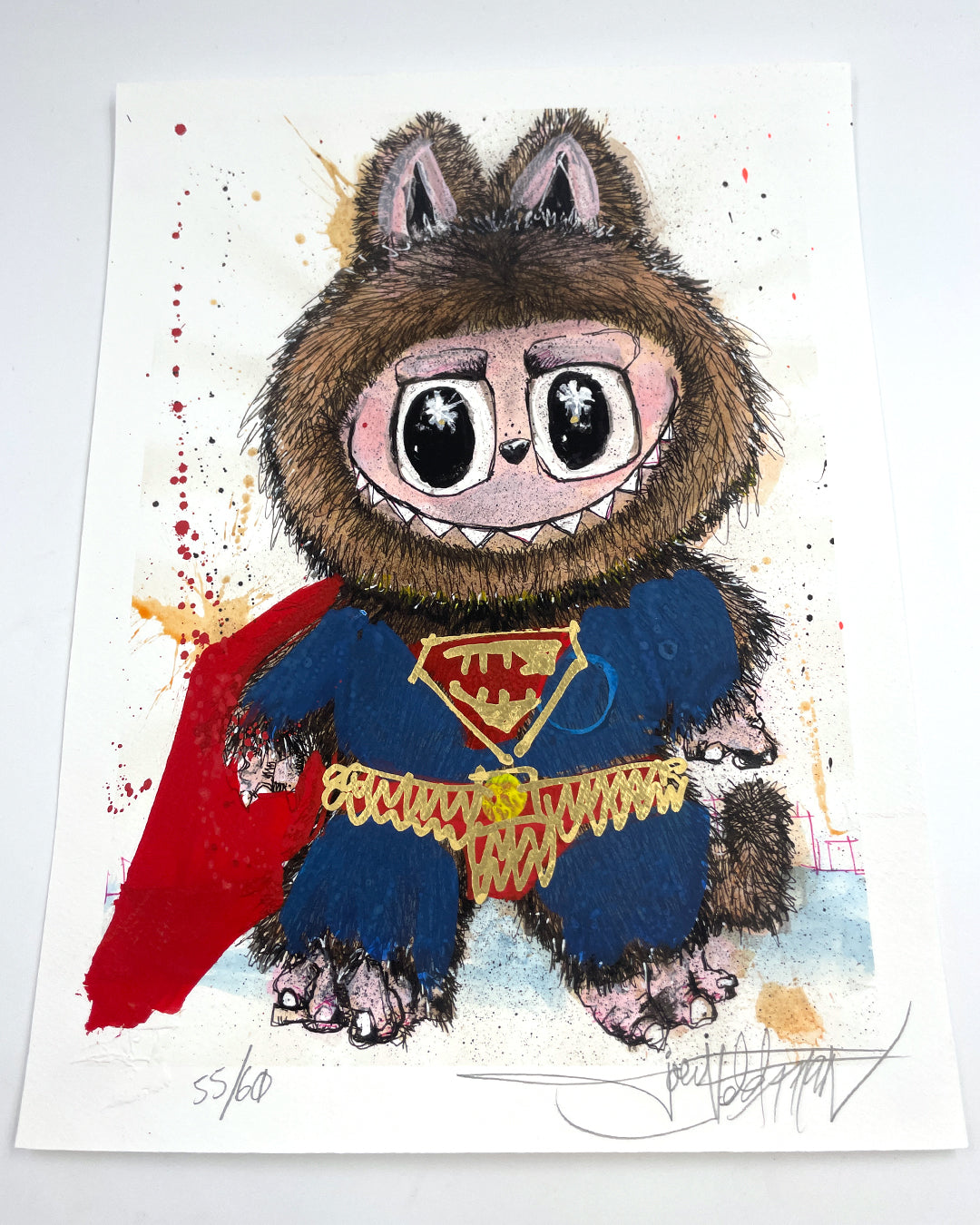 A whimsical Joey Feldman print shows a furry, wide-eyed creature in a superhero costume on paint-splattered paper—available as an archival pigment print with hand-painted embellishments.