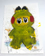 A whimsical Joey Feldman painting features a fuzzy yellow monster with big eyes, red cheeks, and a toothy grin on a white background with colorful splatters and hand-painted embellishments.