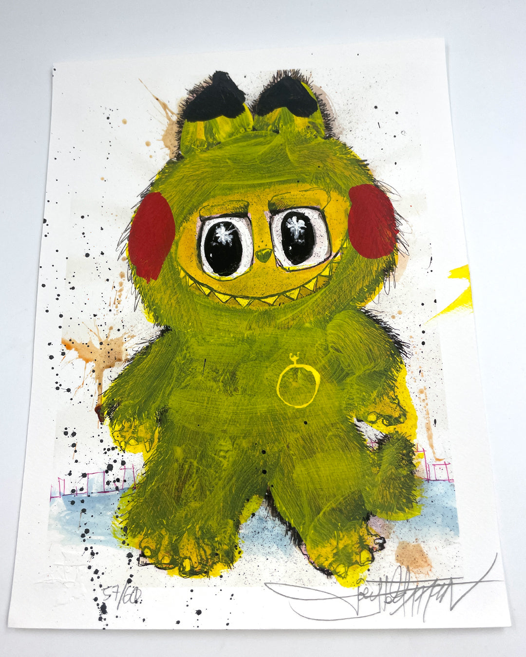 A whimsical Joey Feldman painting features a fuzzy yellow monster with big eyes, red cheeks, and a toothy grin on a white background with colorful splatters and hand-painted embellishments.