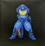 A stylized, cartoon-like character in blue armor with an arm cannon stands against a black textured background—a Joshua Budich tribute to Megaman art for a video game inspired exhibition.