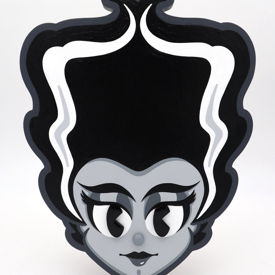 Stylized cartoon portrait of a woman with a tall, black beehive and white streaks, acrylic on wood. She has large eyes, long lashes, red lips, and a gray face on a white background. By Miles Ritchie for Spoke Art's 15th Anniversary Show.
