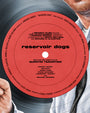 A suited man’s hand holds a vinyl record with Reservoir Dogs credits in black and red text, set against a light blue background reminiscent of Super Sounds of the Seventies in this archival pigment print by Neil Davies.