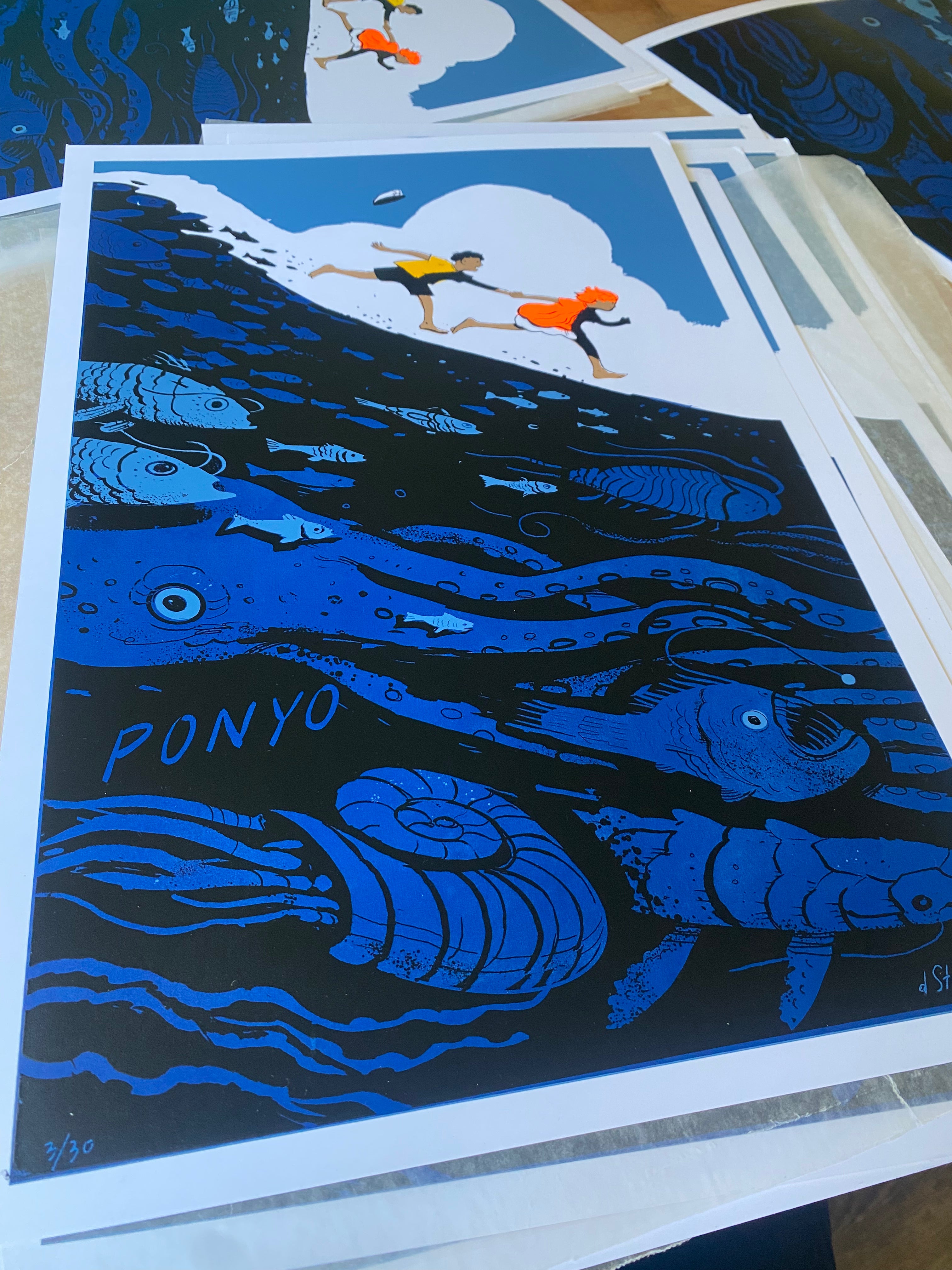 A vibrant Dean Stuart screen print shows two children running over the sea, diverse ocean life below, and "PONYO" underwater. Blue tones with orange highlights celebrate Spoke Art's 15th Anniversary.