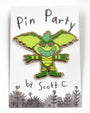 A green, cartoon-style gremlin hard enamel pin with pink eyes is displayed on a card that features the Scott C. brand name and playful flower doodles along the bottom, accentuating this delightful gold metal plated accessory.