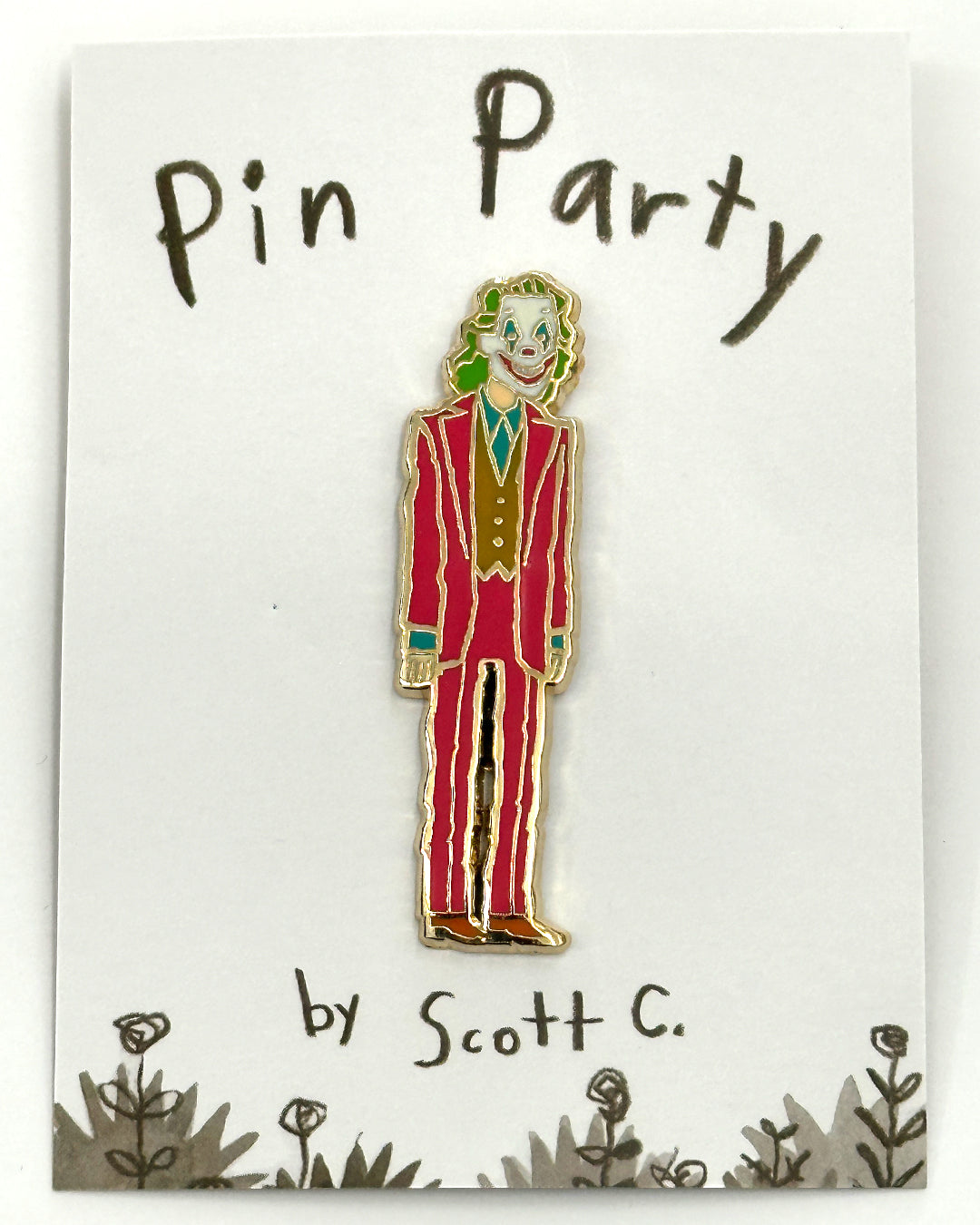 A vibrant hard enamel pin by Scott C. shows a character in a red suit, green hair, and clown makeup on a “Pin Party by Scott C.” card with flower doodles. Gold-plated metal; limited edition.