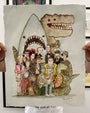 A person holds a limited edition archival pigment print by Scott C. featuring cartoon versions of iconic movie characters—shark, dinosaurs, aliens, and humans—posing for a group photo. Signed by the artist.