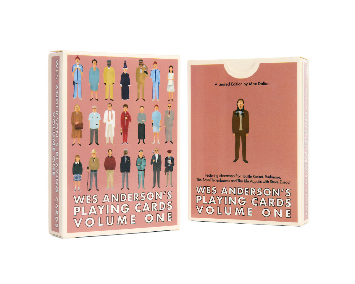 Two boxes of Max Dalton’s Playing Cards Volume One are shown. Beautifully custom-designed playing cards by Max Dalton, the boxes feature illustrated characters from Wes Anderson films on a pink background, with text on the front and back.