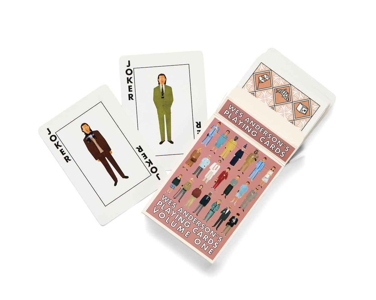 Two playing cards labeled JOKER showcase illustrated men in suits. The open box beside them, branded Max Dalton, reads Wes Anderson’s Playing Cards Volume One and features illustrated characters on the cover, reflecting custom designed playing cards created by Max Dalton.