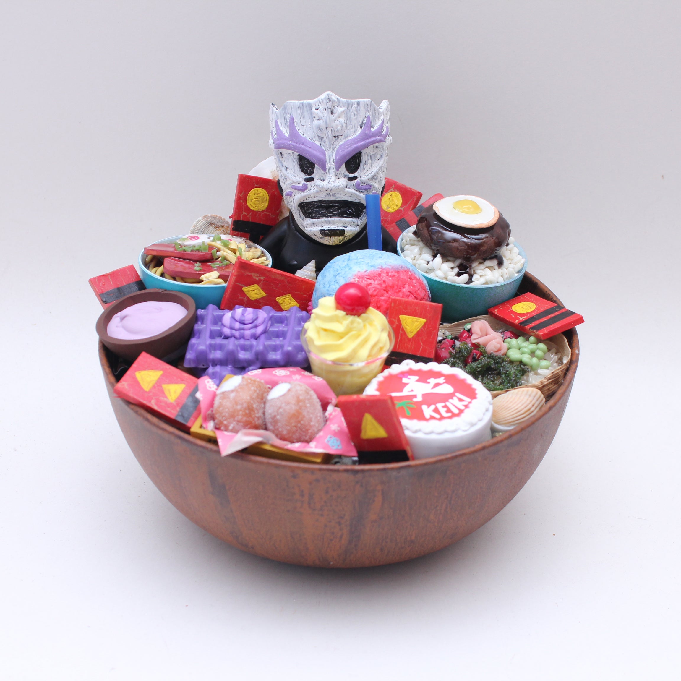 A Zard Apuya-inspired wooden bowl filled with colorful miniature cupcakes, mochi, sushi, sweets, and a purple mask centerpiece—an eye-catching display piece perfect for San Diego Comic-Con 2025!.