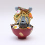A Zard Apuya gray bear figurine, inspired by Kidrobot Munny toys, sits in a red ramen bowl filled with toy noodles, veggies, and egg, looking surprised against a plain white background.