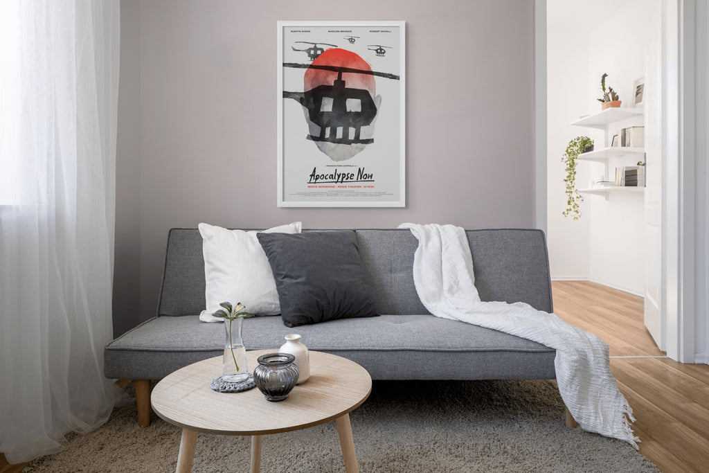 Photo of Aleksander Walijewski's Apocalupse Now print in a black frame on a gray wall in a living room with a dark gray couch in front of it and a small round table and a window with white curtains