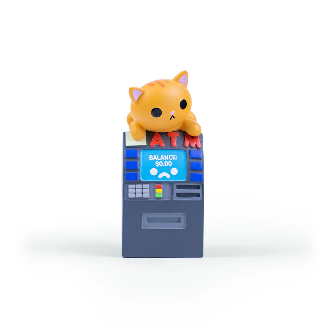 A cute orange cat figurine from the 100% Soft Bodega Kitties vinyl figure blind box series sits atop a toy ATM displaying a balance of $0.00. The ATM features red "ATM" letters and a blue screen, all set against a plain white background.