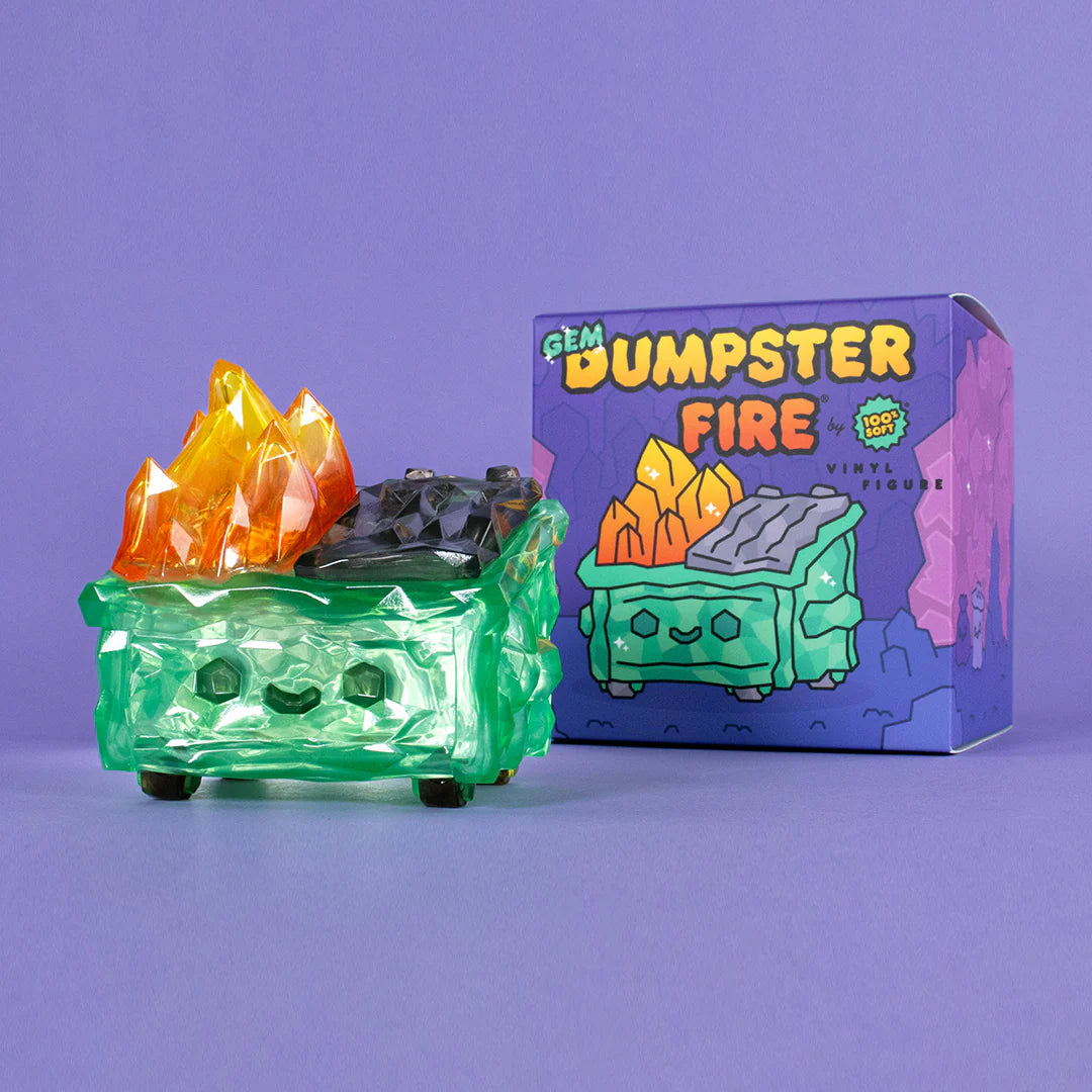A translucent green vinyl figure from 100% Soft, featuring orange-yellow crystal flames and a smiling face, sits by its colorful "Gem Dumpster Fire" box on a purple surface.