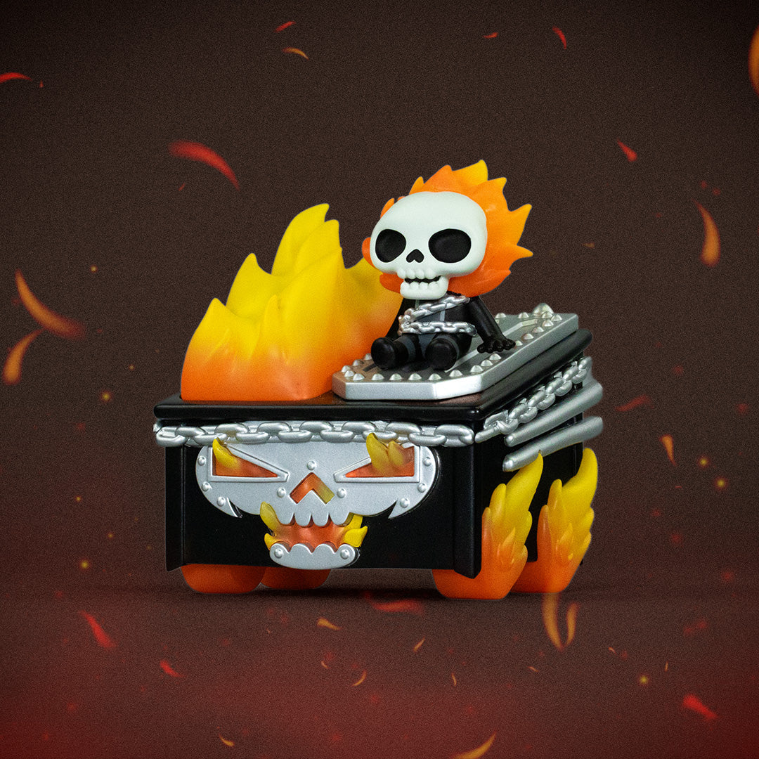 A skeleton figure with fiery hair sits atop a flaming, chained box featuring a skull-face design, reminiscent of the 100% Soft Ghost Rider Dumpster Fire vinyl figure from Marvel, surrounded by floating embers against a dark background.