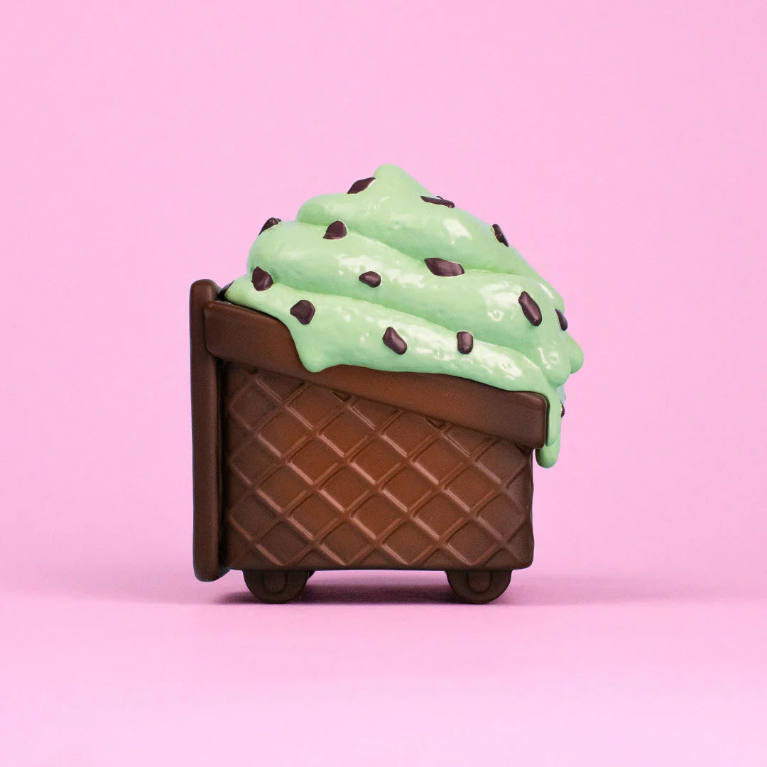 A playful 100% Soft Mint Chip Vinyl Figure, shaped like a chocolate waffle ice cream cone filled with mint green ice cream and chocolate chips, sits against a pink background—bringing sweet vibes to any space.