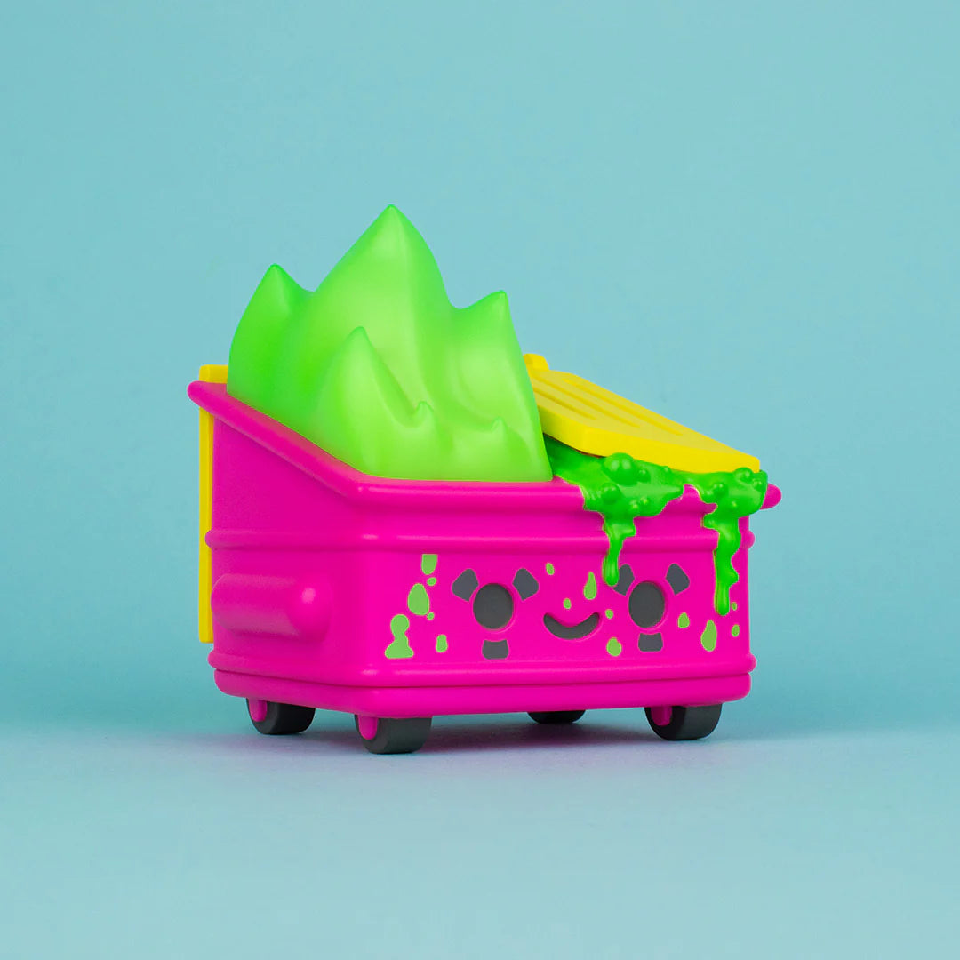 A 100% Soft bright pink vinyl Dumpster Fire figure featuring a smiling face and overflowing with toxic green slime and yellow trash, displayed against a plain light blue background.